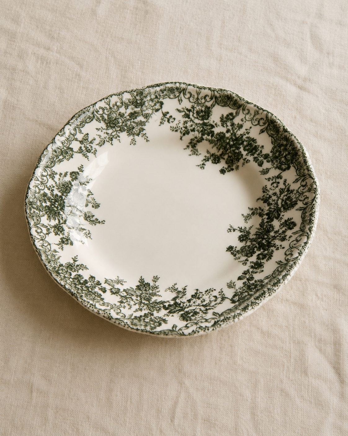 Green floral transferware plate resting on rumpled natural linen