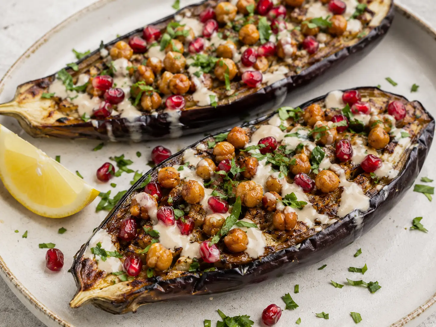 Two roasted eggplant halves loaded with crispy chickpeas, tahini, pomegranate seeds and parsley