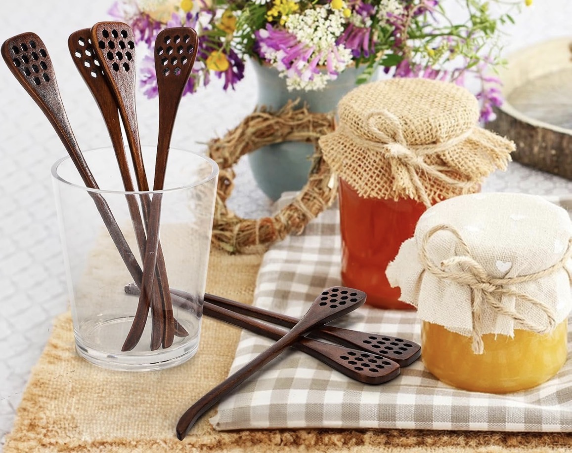 Small jars of honey covered in linen and burlap beside carved wooden honey sticks